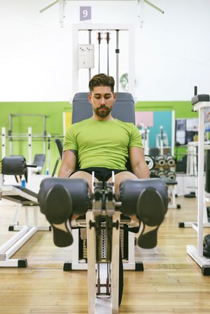 Fit male in green t-shirt working out quads using gym equipment