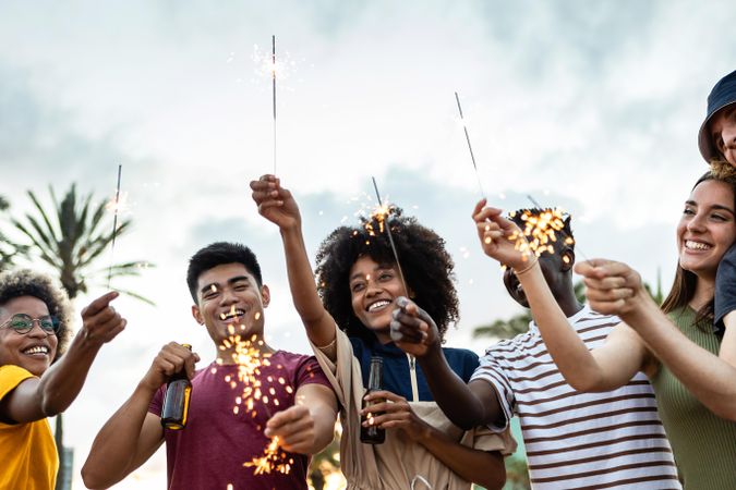 Group of united multiracial friends laughing and celebrating with sparkles outdoors