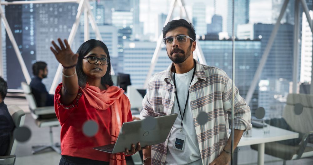 Female and Male Indian Financial Advisers Use Laptop Computer to Discuss a Stock Market Strategy in a Modern Company.
