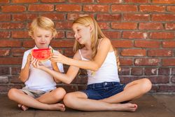 Cute Young Boy and Girl Eating Watermelon Against Brick Wall