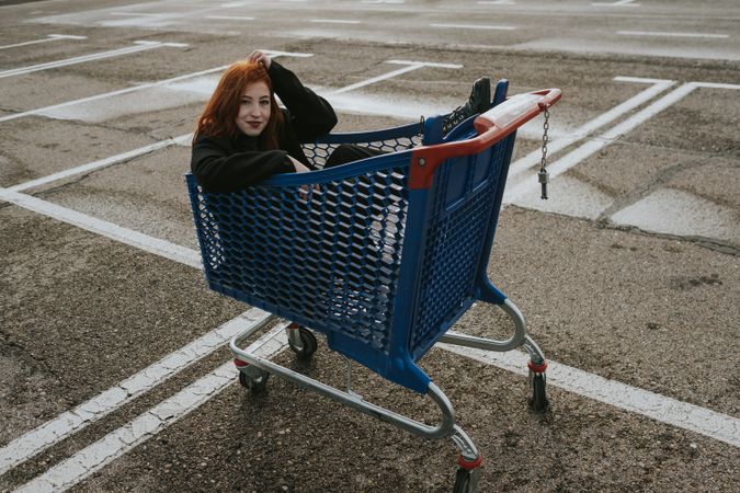 Smiling woman sitting in shopping trolley in parking lot