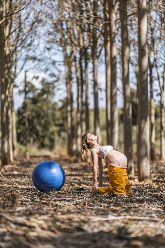 Adult pregnant woman training with pilates ball in park during sunny day