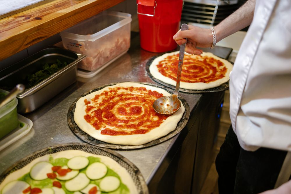 Pizza man adding tomato sauce to pizza