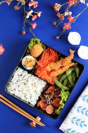 Japanese Bento Lunch Box with Rice, Sausages, Nugget, Edamame, Carrot Salad, and Shrimp Tempura
