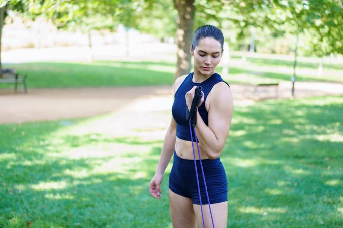 A woman exercises with resistance bands in a park, showing determination and focus on her outdoor workout