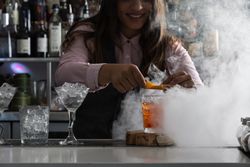 Bartender squeezing orange peel over a Negroni cocktail 4AXKY5