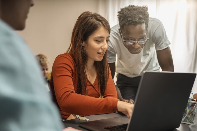 Young woman and Black man collaborating at laptop in modern workspace with warm light and focused teamwork