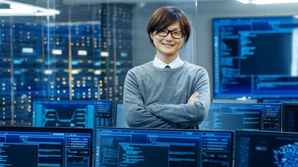 In the System Control Room IT Technician Crosses Arms and Smiles.