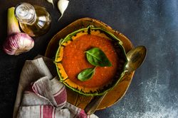 Green and orange ceramic bowl of gazpacho soup with basil leaves and garlic