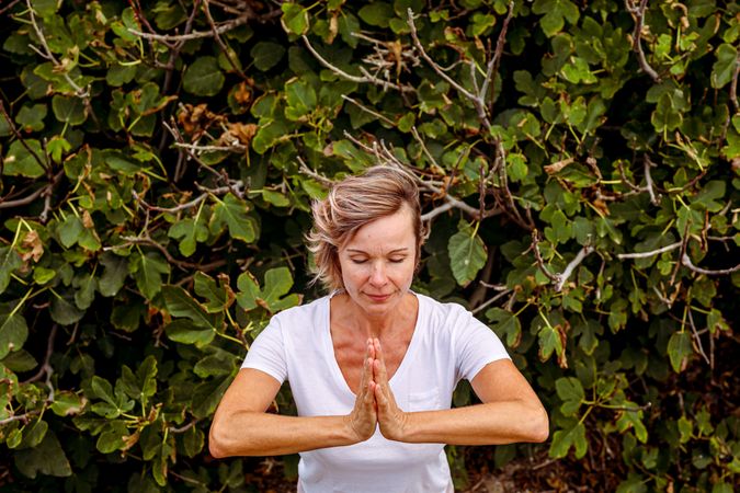 Adult woman meditating near bush