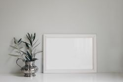 Horizontal wooden picture photo frame on table next to olive twig in vintage silver vase