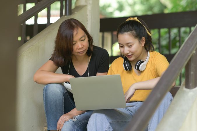 Two women using laptop on the stairs of the house, work from home.