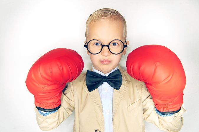 Serious blond boy wearing round glasses and red boxing gloves