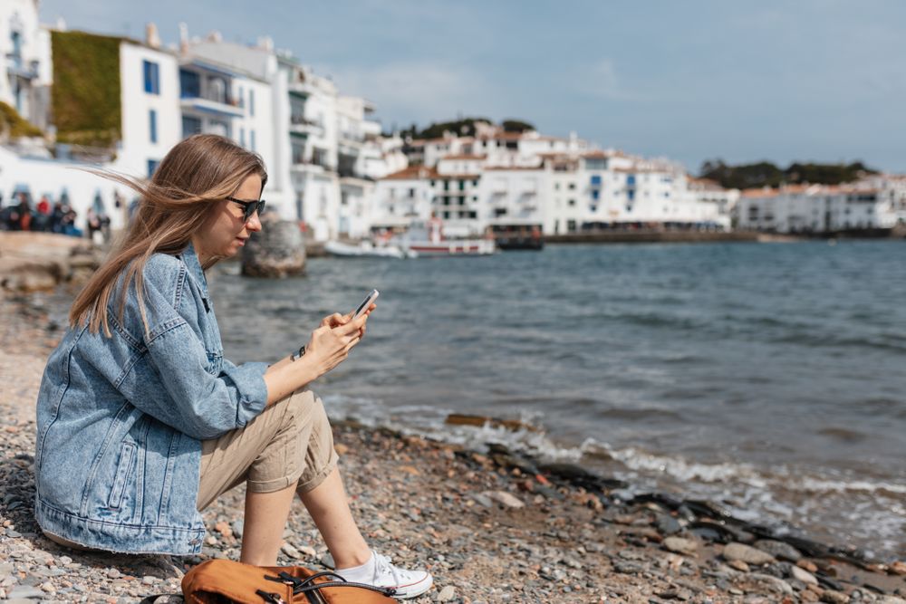 Young woman sitting by the water with wind blowing in her hair