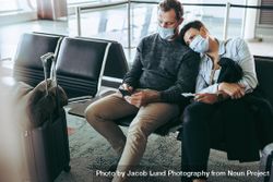 Couple with face masks sitting in waiting area at airport 41Pol5