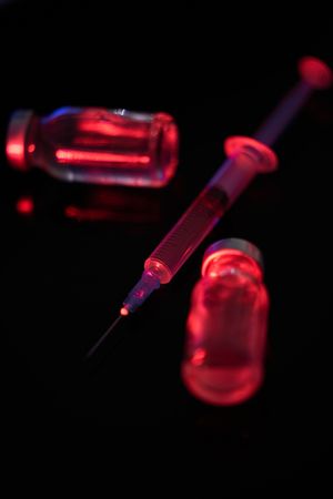 Syringe with vaccine near glass bottles in darkness