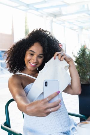 Smiling Black woman with baby clothes taking selfie on smartphone