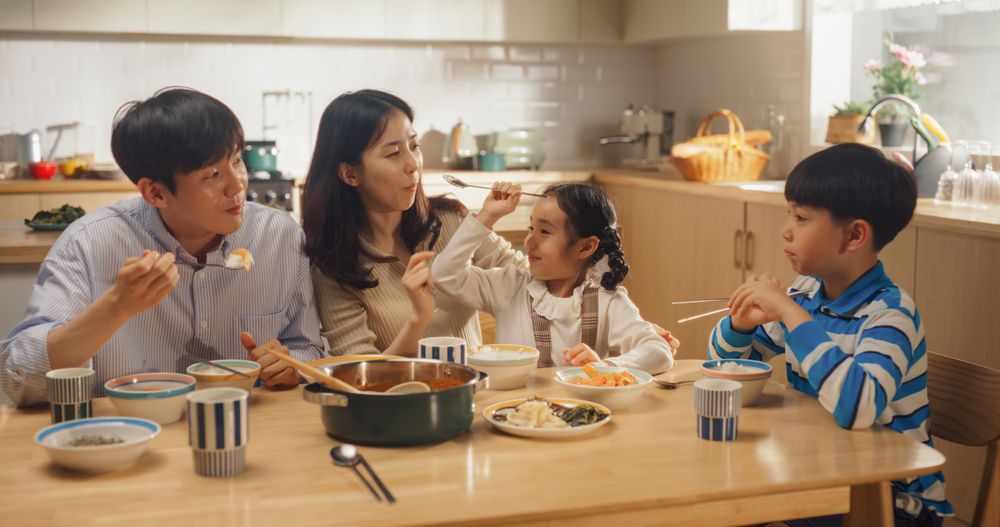 Happy Korean Family of Four Enjoying a Delicious Meal Together in Their Kitchen at Home.