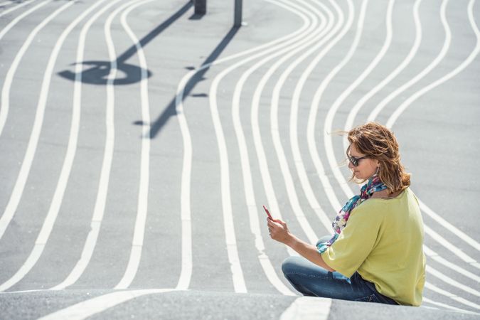 Modern relaxed woman on marked road and browsing smartphone