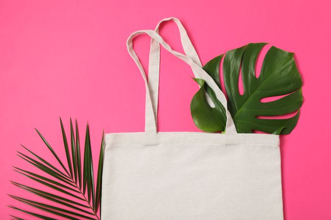 Eco bag and palm leaves on color background, top view