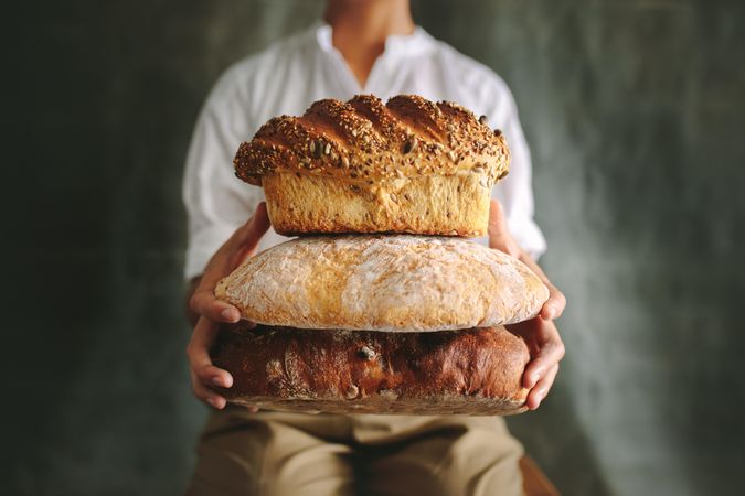 Cropped shot of baker showing various types of loaf bread against gray background