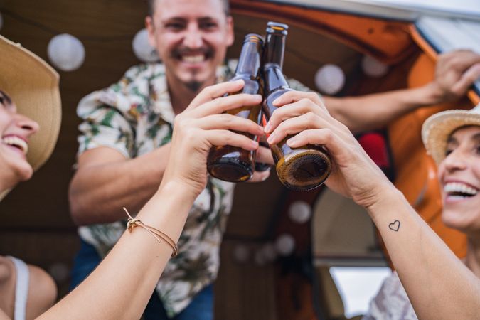 Smiling friends clinking bottles of beer celebrating vacation