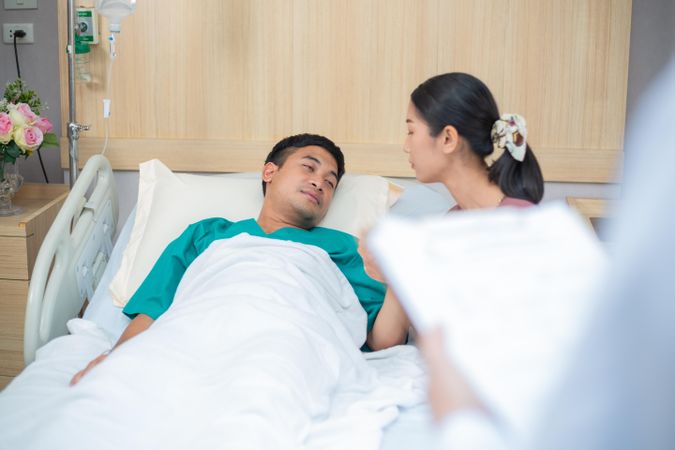 Couple in hospital with male in bed with doctor with clipboard