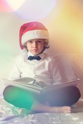 Bored boy in Santa hat reading book