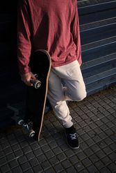 Crop skater leaning on wall on city street