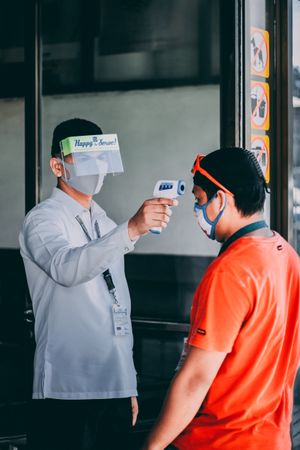 Security guard using thermometer on customer's head to measure his temperature