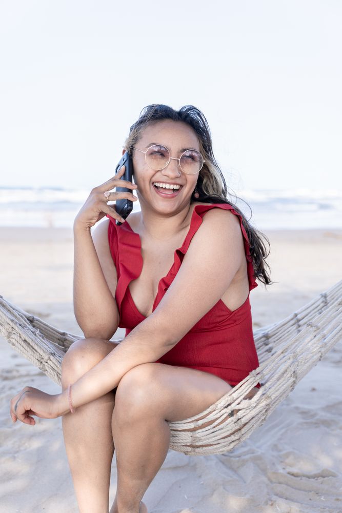 Hispanic woman is laughing during a phone call on a hammock at the beach
