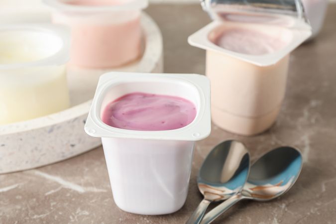 Composition with plastic cups with yogurt on grey table, space for text