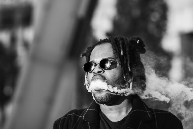 Black man exhaling cloud of smoke on street