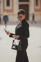 Stylish Black woman with handbag and smartphone on street
