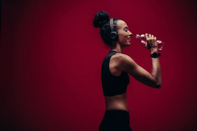 Fitness woman drinking water on red background