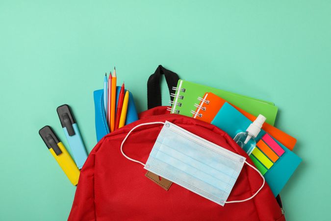 School supplies with medical mask and sanitizer on mint background