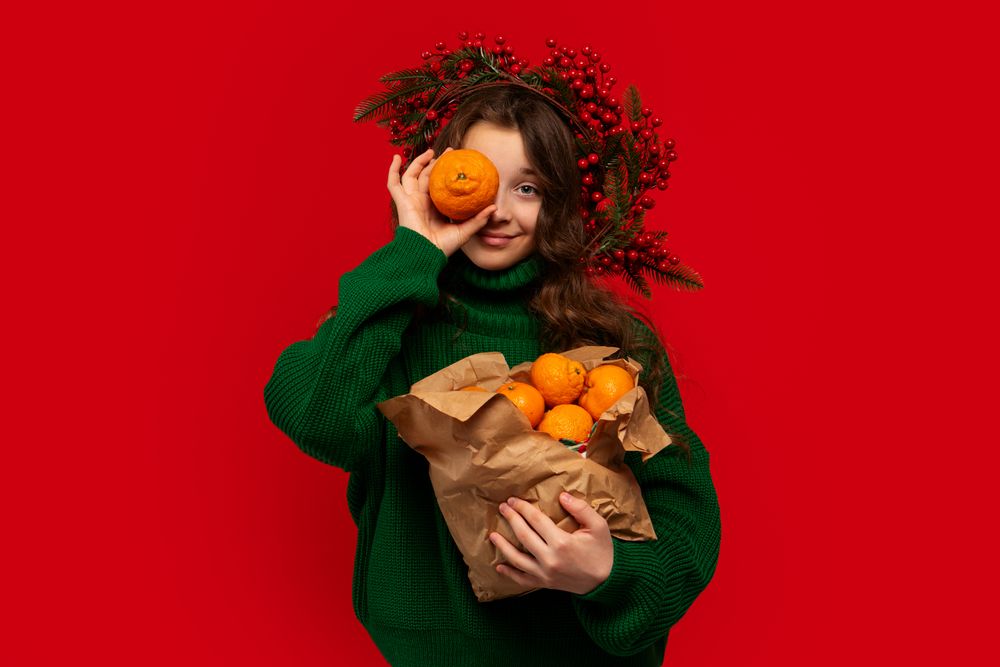 Young girl in green sweater holding paper bag of oranges