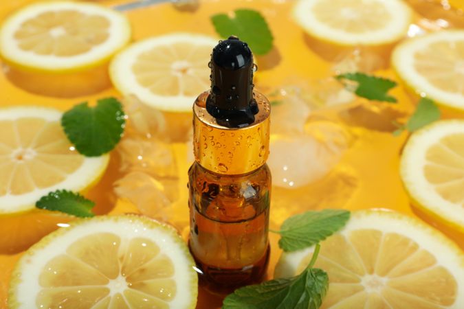 Lemon slices floating in water with mint slices, ice and cosmetic bottle