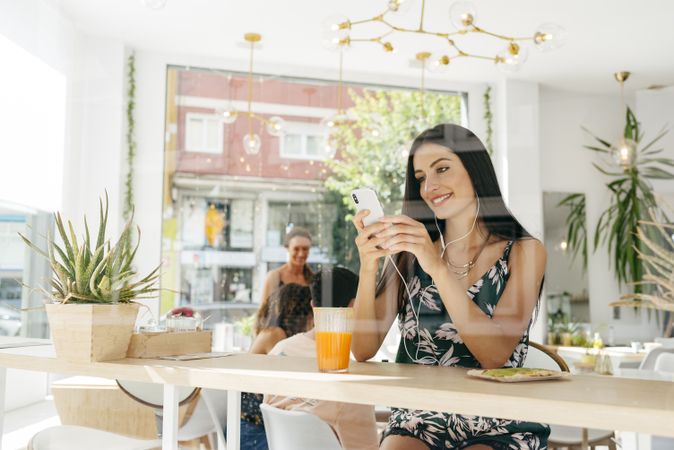 Woman with healthy drink listening to music in cafe