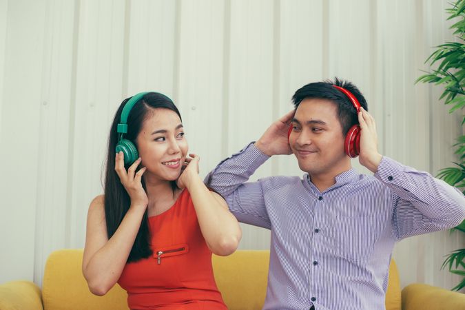 Male and female having fun listening to headphones on yellow couch