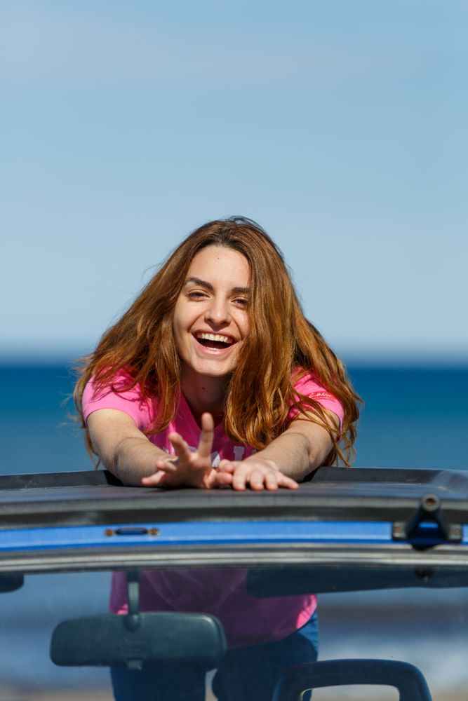 Smiling woman leaning on roof of car