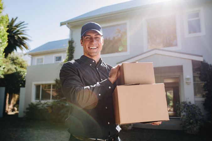 Delivery man standing in front of a house holding two cardboard boxes