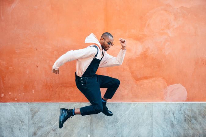 Male in overalls and hoodie jumping in front of wall