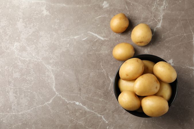 Top view of dark ceramic bowl full of potatoes on marble counter, copy space