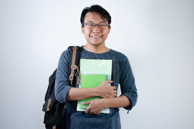 Asian young male student wearing bag and carrying books smiling and happy expression