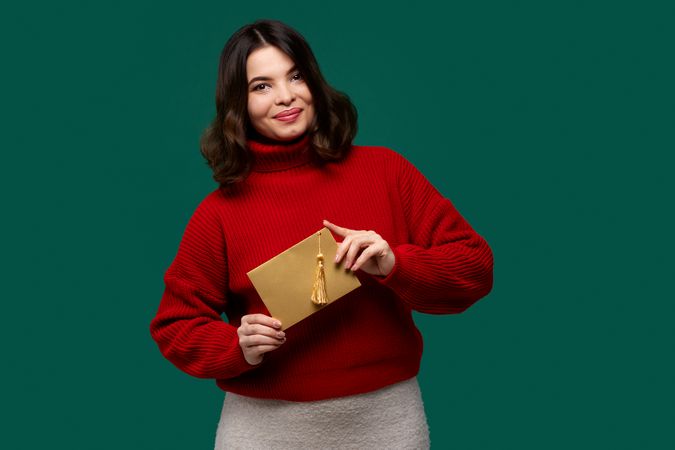 Smiling woman in red sweater holding golden envelope with tassel