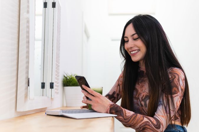 Woman on mobile phone taking notes in notebook and speaking on mobile phone sitting in bar with healthy beverage