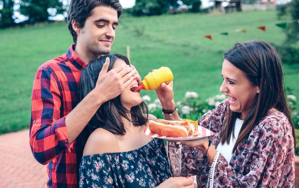 Man holding friend's eyes closed as friends do a funny taste test