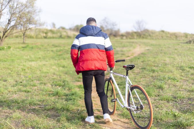 Rear view of a young man walking in a park with a bike