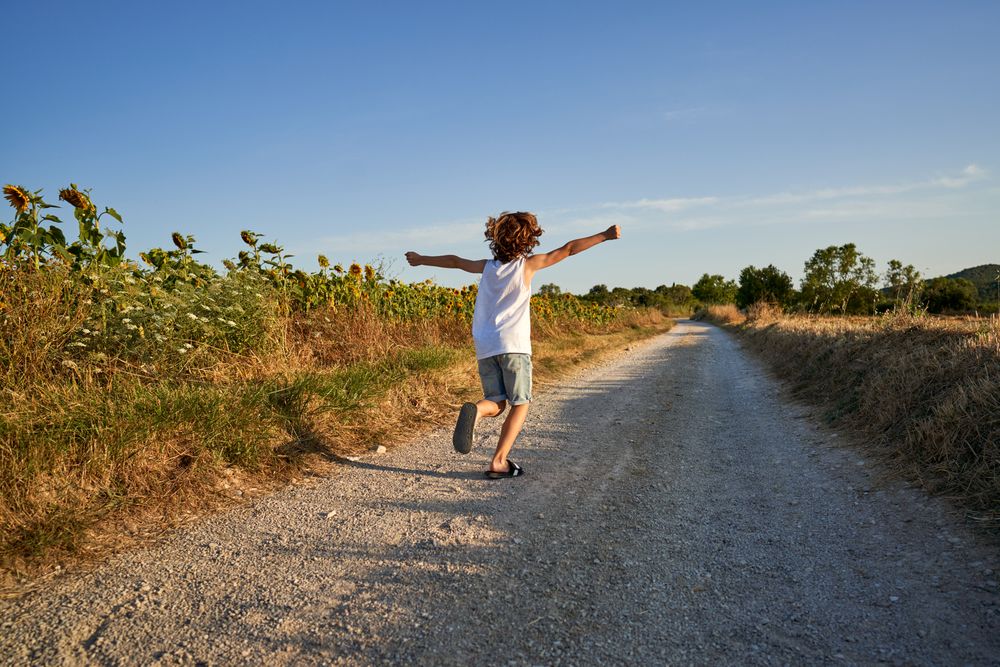 Unrecognizable boy running along endless road in countryside